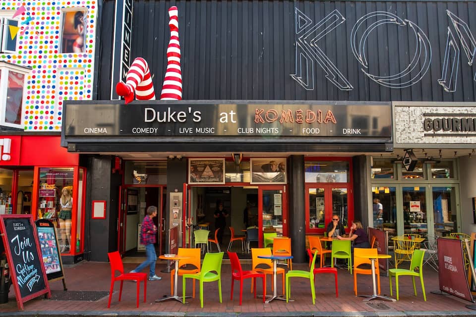 Duke's at KOMEDIA with colorful chairs outside and a sign for Gourmet Burger Kitchen.