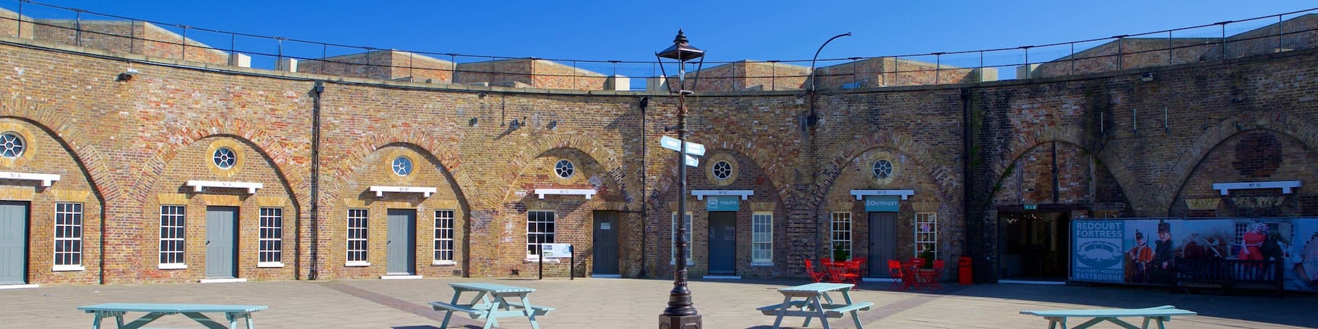 A historic brick building with arched windows and doors, picnic tables, and a red brick plaza.