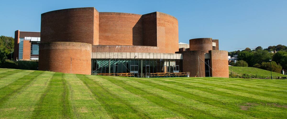 A modern building with cylindrical structures and a grassy lawn in front.