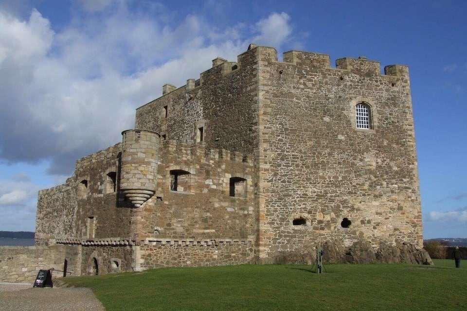 Un grand château en pierre, doté de nombreuses tours et de fenêtres en arc.