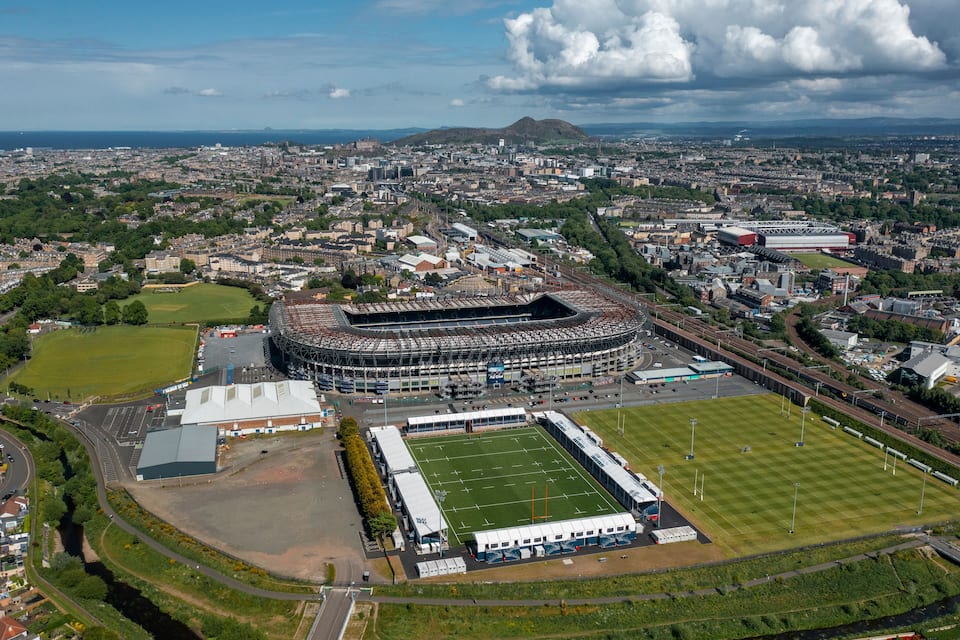 An aerial view of a stadium surrounded by urban buildings and a river.