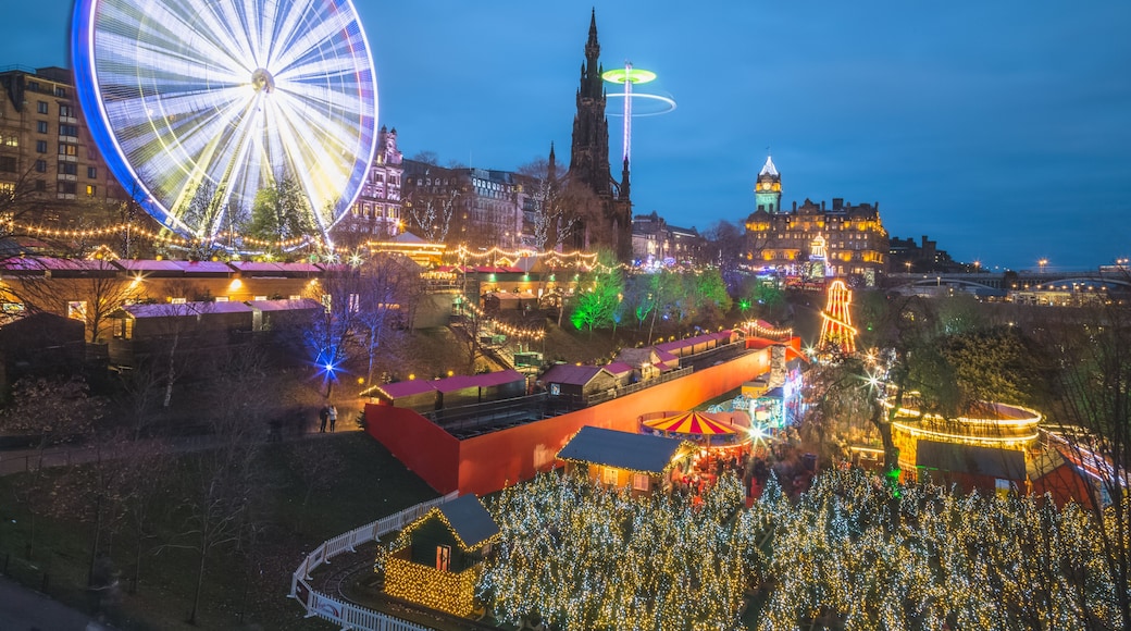 A vibrant and lively view of the Edinburgh Christmas Market at Princes Street Gardens in Scotland at night all lit up and illuminated with Christmas lights.