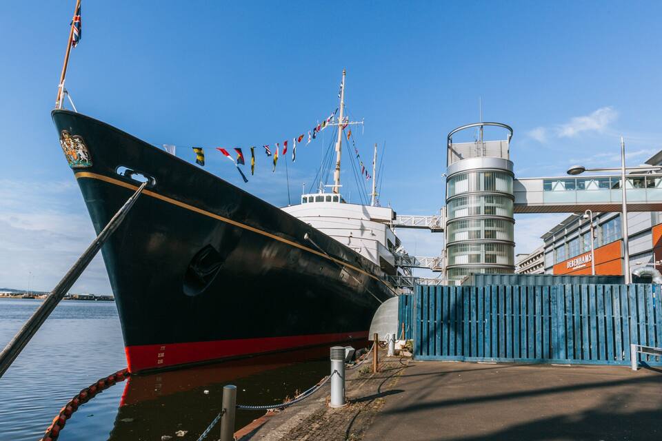 Un grand navire était amarré dans un port, avec une clôture bleue et un bâtiment moderne en arrière-plan.