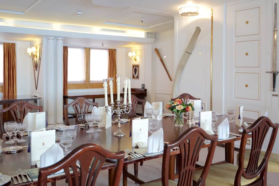 A formal dining room with wooden furniture, white walls, and a large window with curtains.