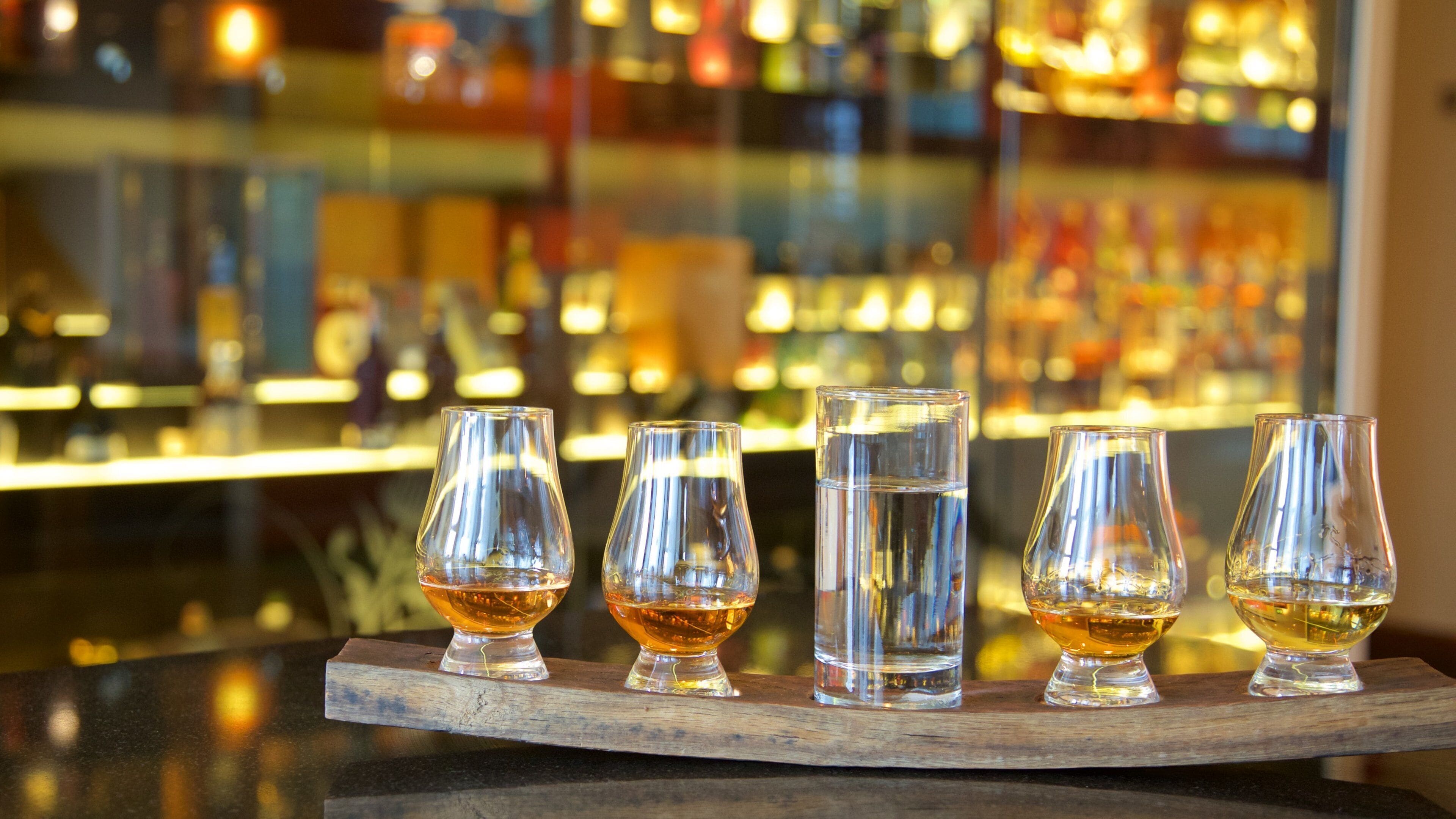 A bar with glasses of whiskey and water on a wooden tray.
