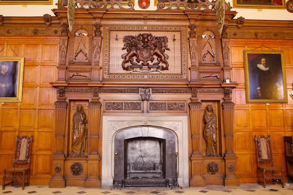 Une cheminée en bois richement décorée, ornée de sculptures complexes et surmontée d’un blason central.