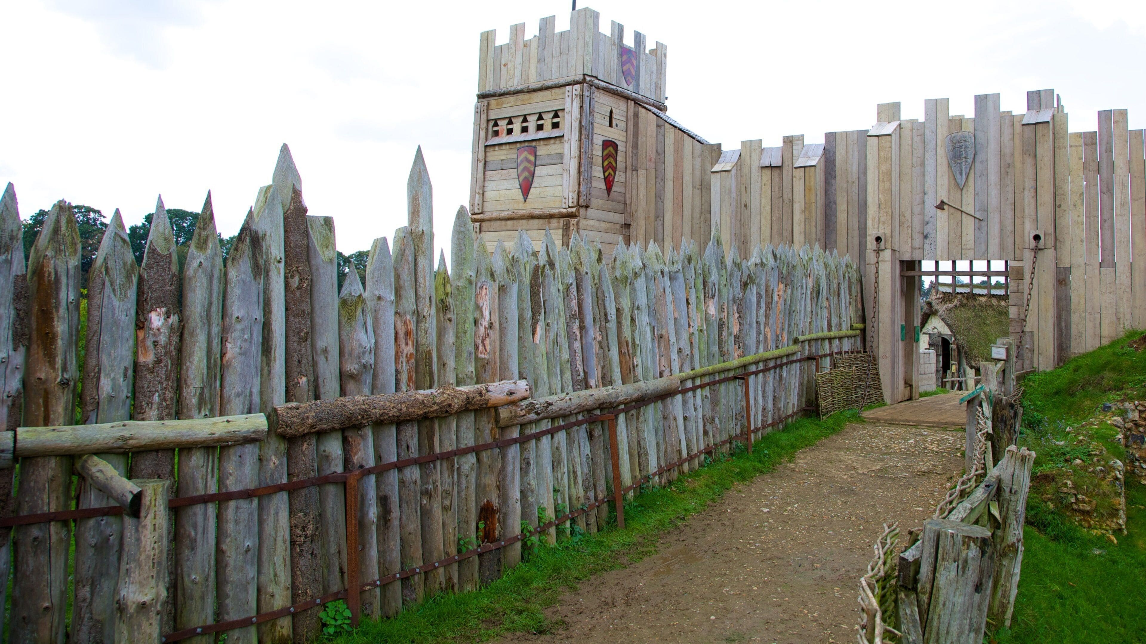 A medieval-style wooden gate with a castle tower and a dirt path leading through it.