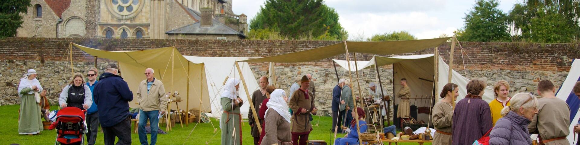 A historical reenactment event with tents, medieval costumes, and a church in the background.