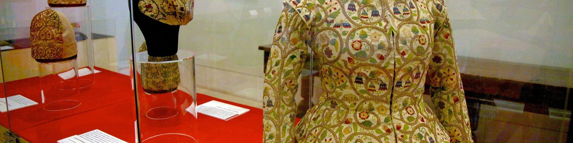 A mannequin in a museum displaying a richly embroidered garment with a red skirt.