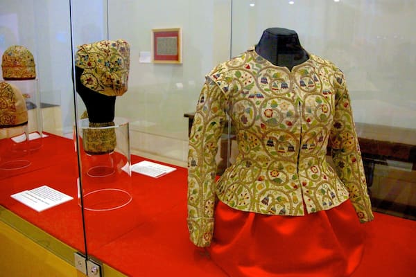 Eine Schaufensterpuppe in einem Museum zeigt ein reich bestickt Kleidungsstück mit rotem Rock.