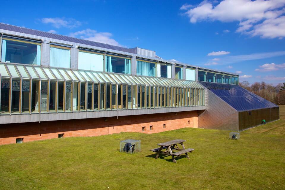Een modern gebouw met grote ramen en een schuin dak, een picknicktafel en een omheind gebied.
