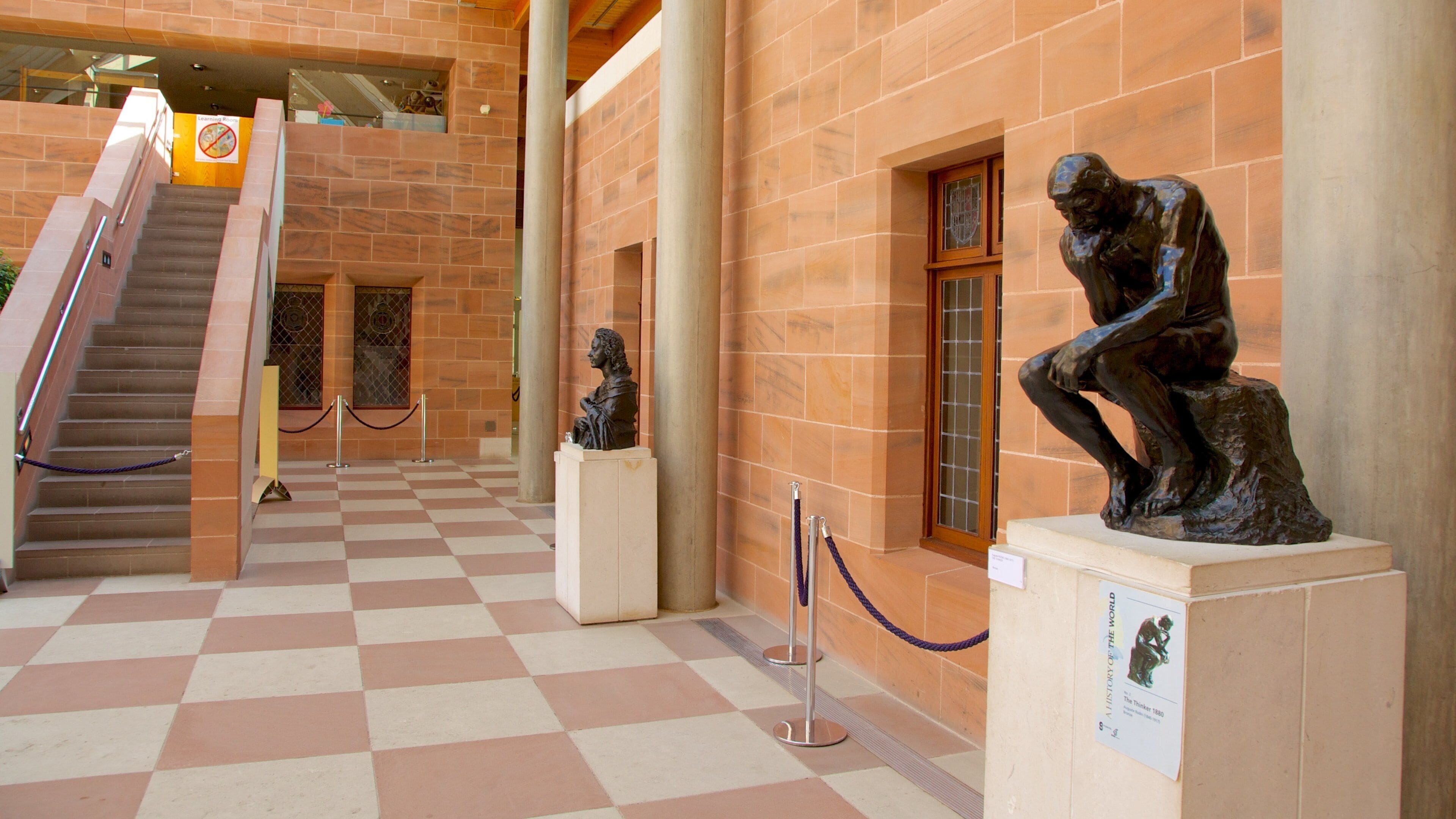 A museum corridor with a checkered floor, a staircase, and two bronze sculptures.
