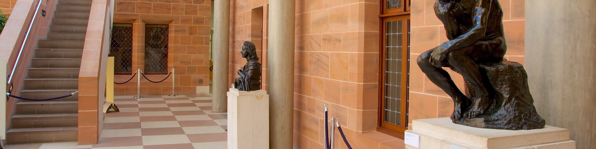 A museum corridor with a checkered floor, a staircase, and two bronze sculptures.