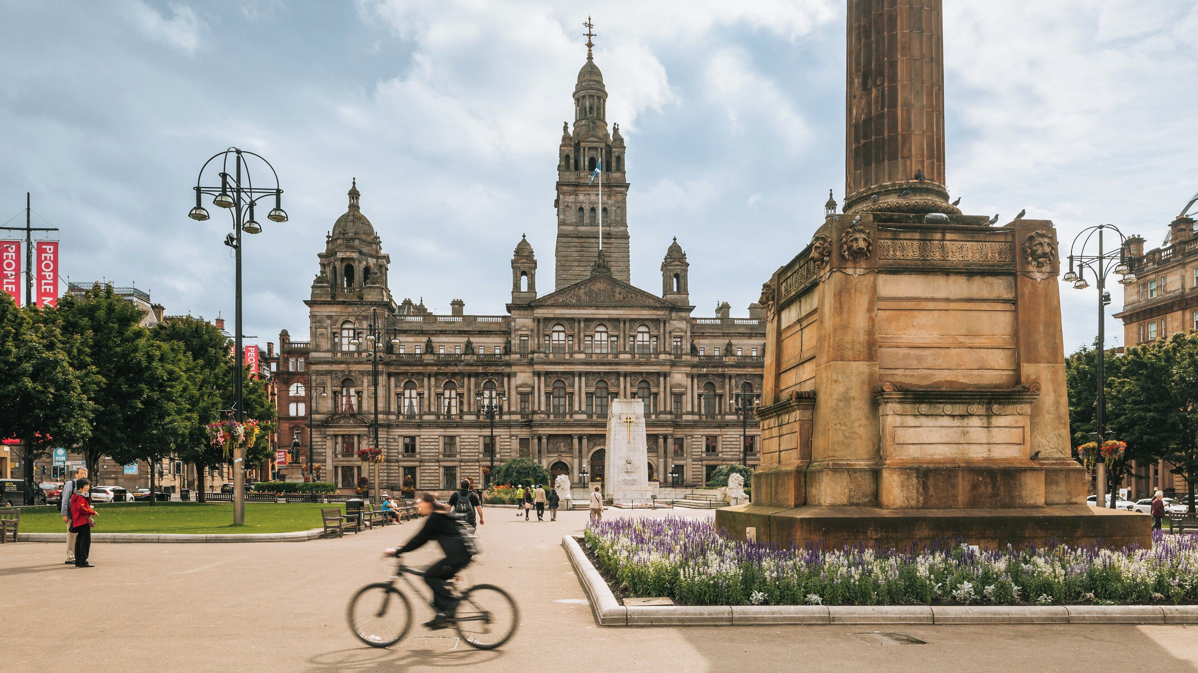 Bicyclist rides through George Square in City Centre Glasgow, showcasing the historic architecture and vibrant atmosphere of Scotland's largest city