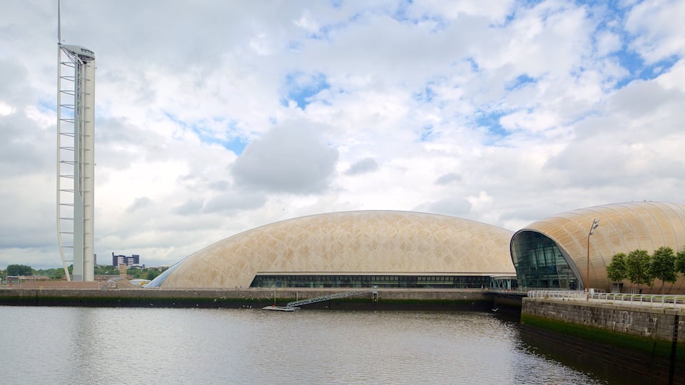 A modern architectural structure with a curved roof and a tall, slender tower beside a body of water.