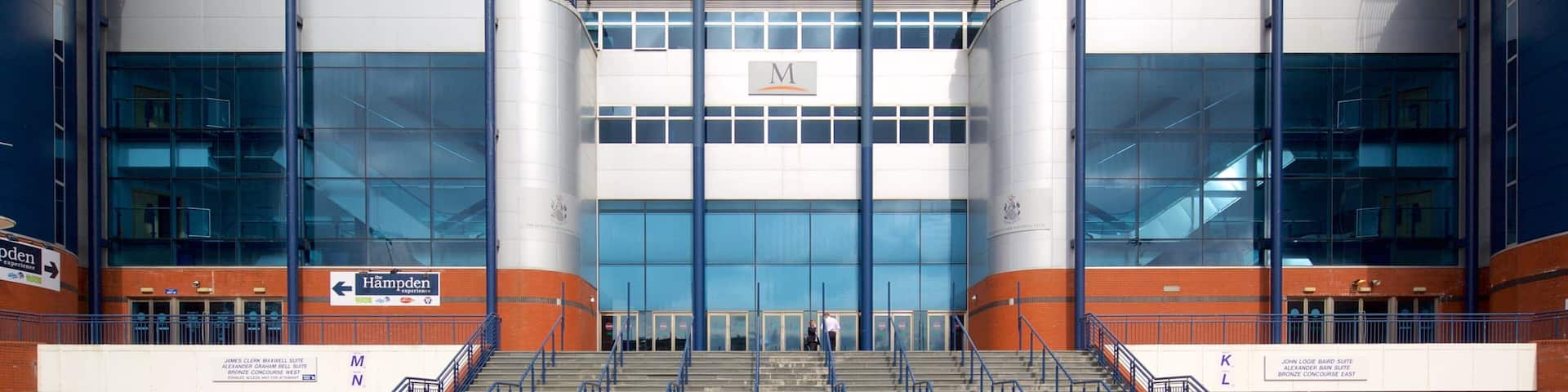 Hampden Stadium's entrance with glass panels, a large 'Hampden' sign, and a staircase leading up to the main entrance.