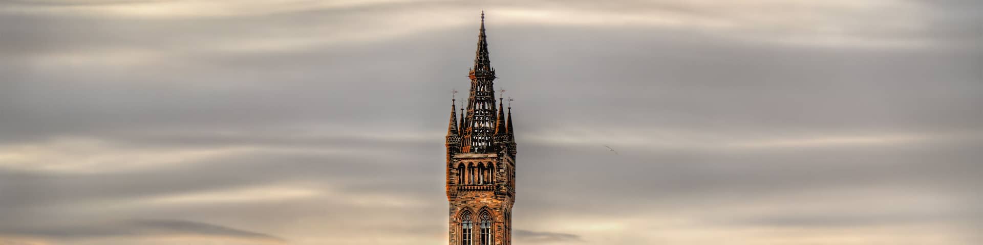 Un edificio histórico con una torre alta y múltiples agujas, rodeado de árboles de colores otoñales.