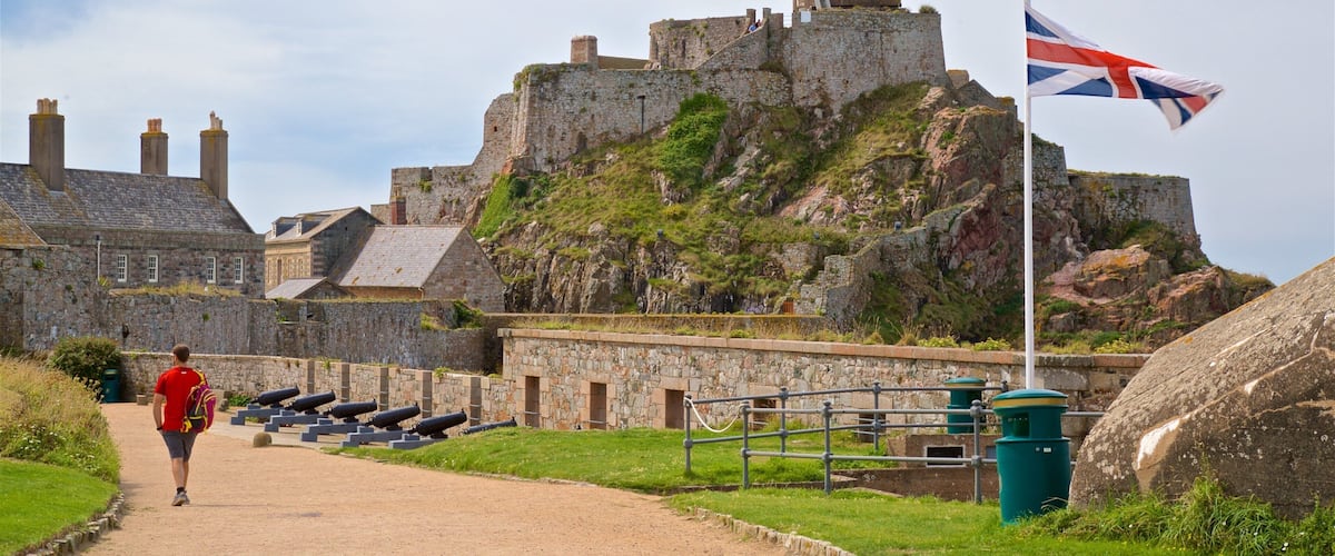 A historic stone fort with cannons, a flag, and a person walking on a path.