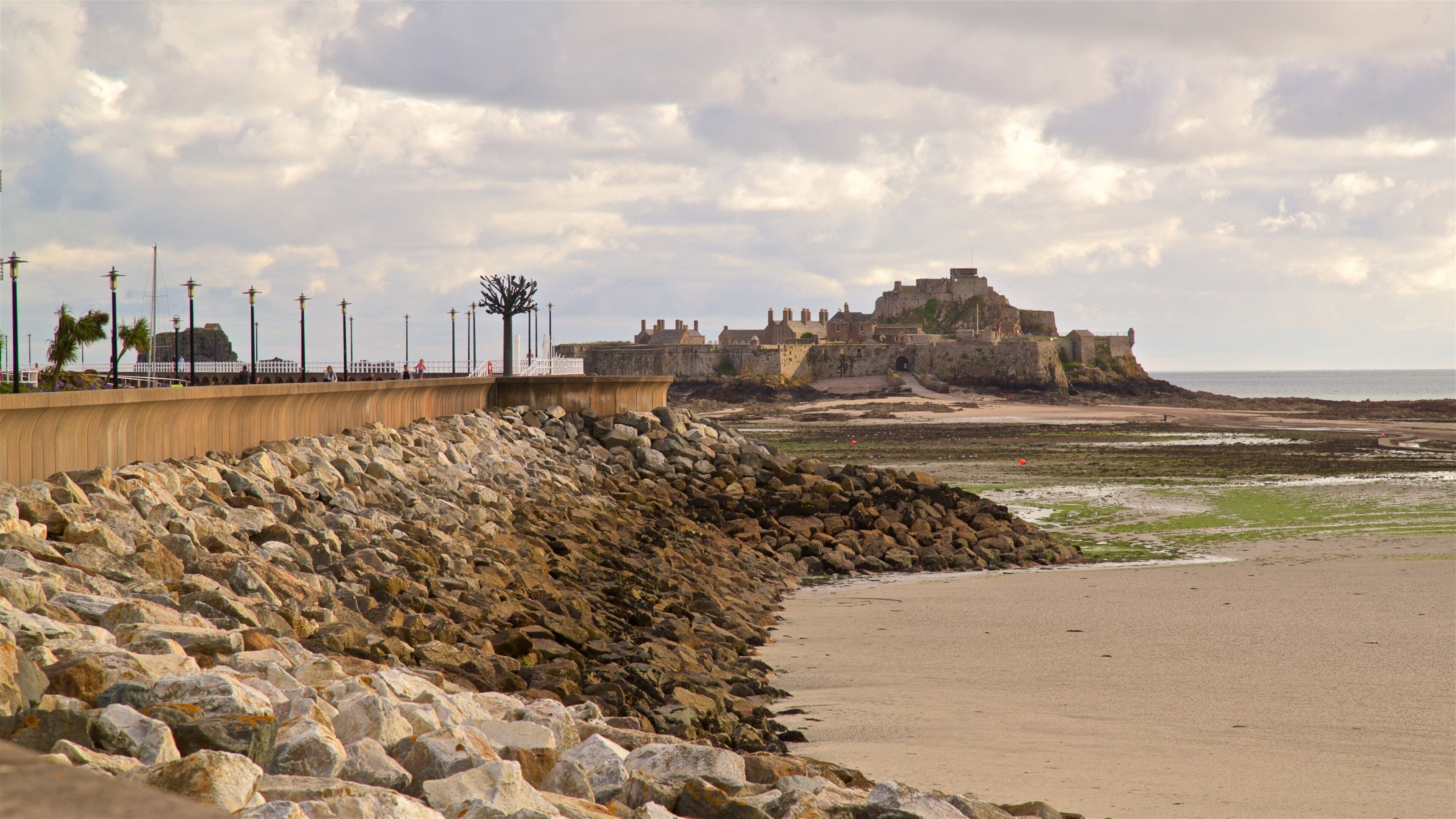 Een rotsachtig strand met een fort en een promenade.