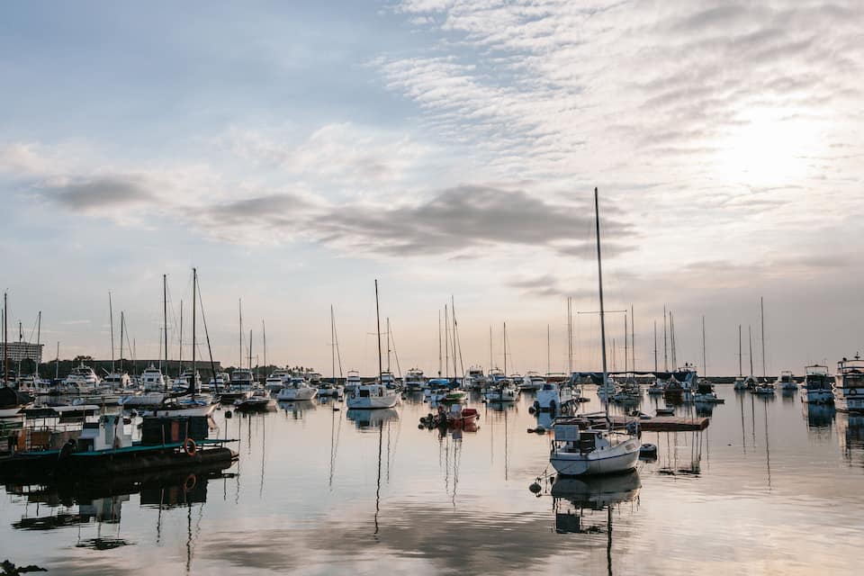 A marina with numerous sailboats docked under a partly cloudy sky.