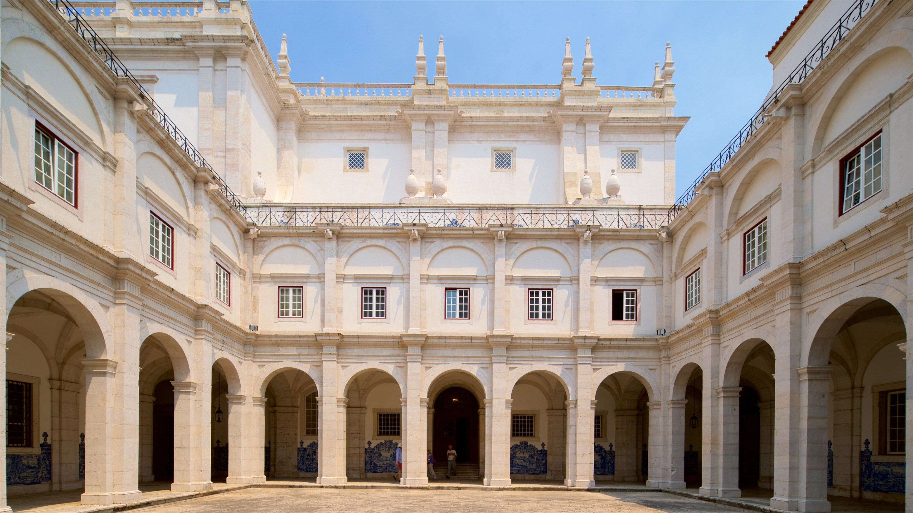 A grand courtyard with a symmetrical building featuring arched walkways and a central entrance.