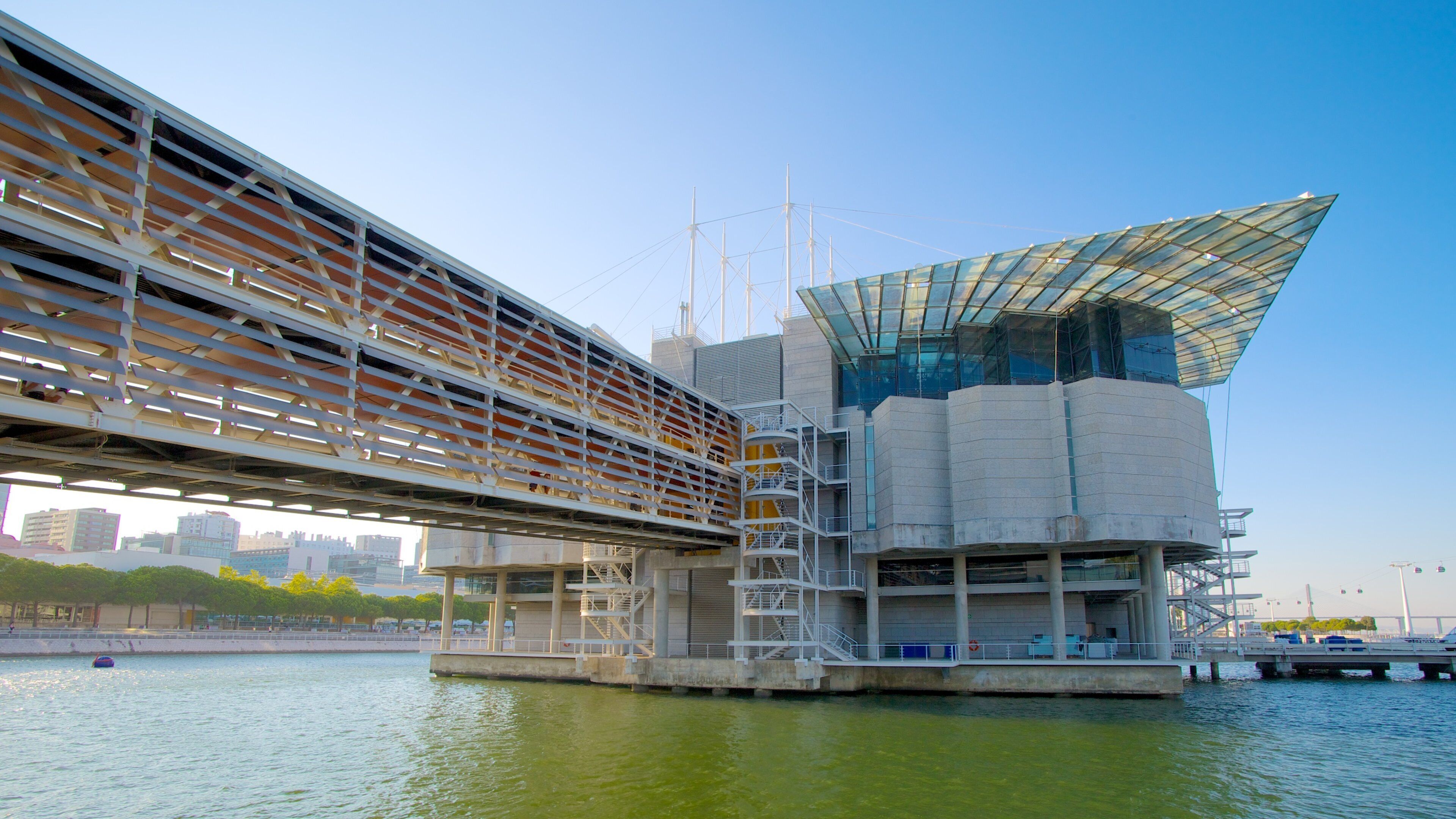 A modern architectural structure with a glass roof and metal framework over a body of water.