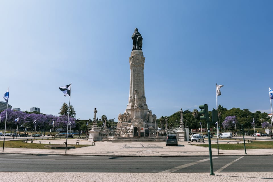 A tall monument with statues, surrounded by flags and trees.