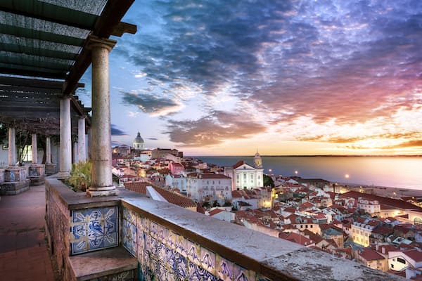 Une vue d’une ville côtière au coucher du soleil, avec un bâtiment remarquable surmonté d’un dôme et une promenade dallée.