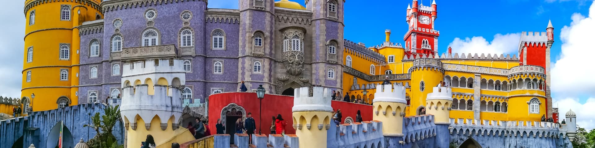 A colorful castle with yellow and purple walls, a red tower, and a blue bridge.