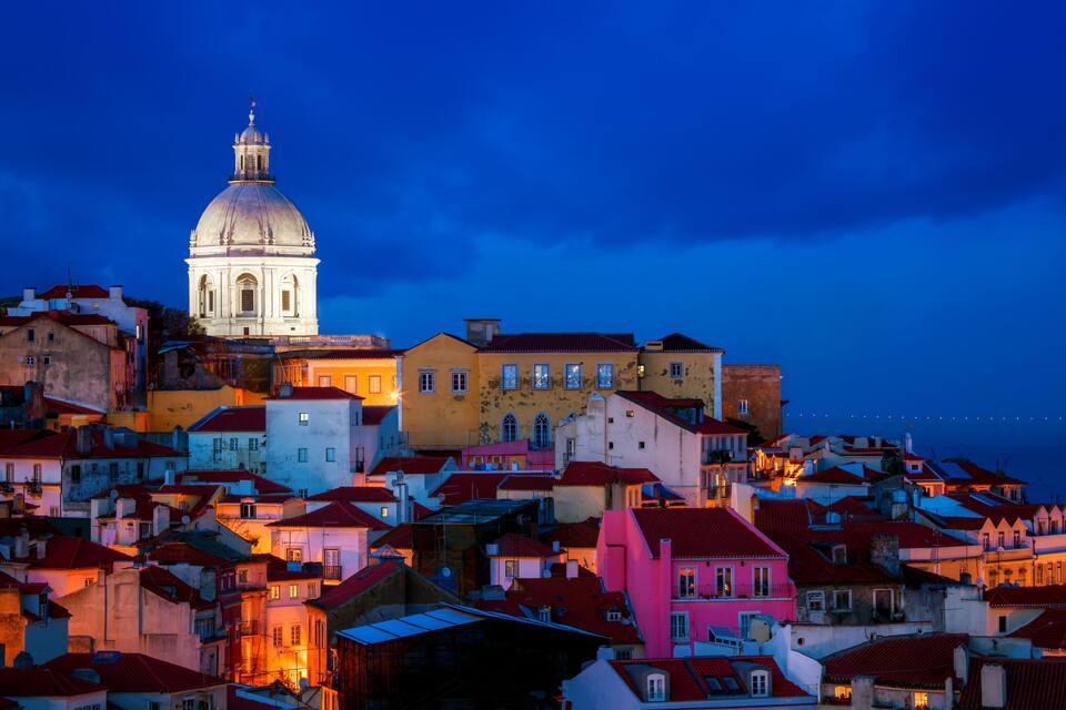 A cityscape at dusk with a prominent white dome building and colorful rooftops.