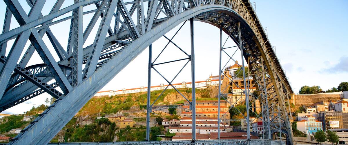 A steel bridge with a river below and buildings in the background.