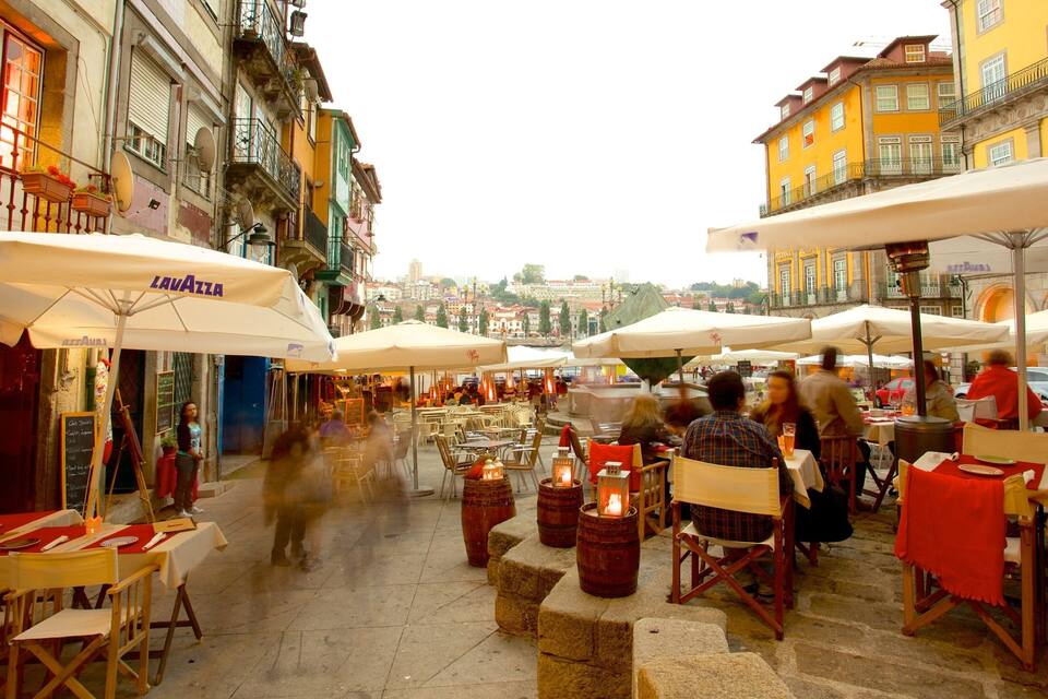 An outdoor café with tables and chairs under umbrellas, set against a backdrop of colorful buildings.