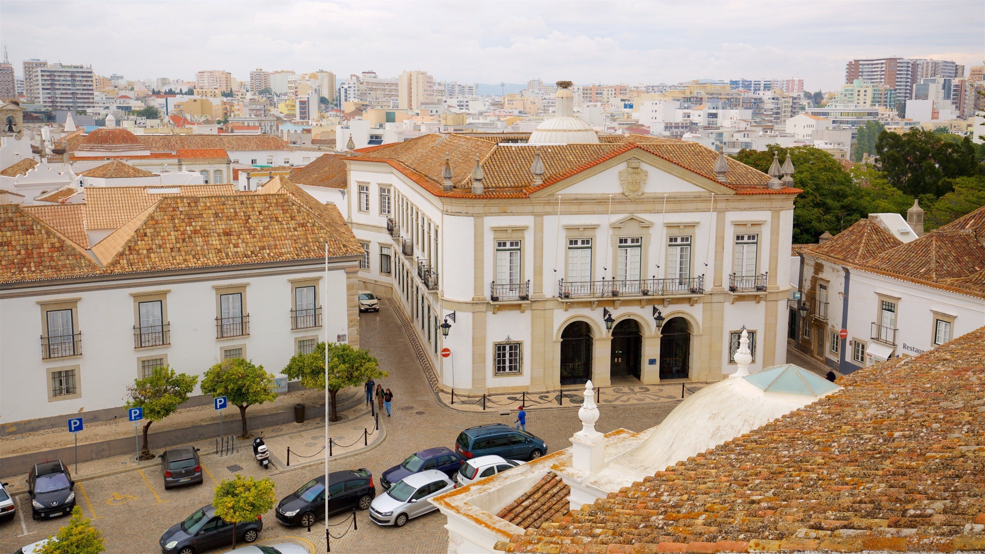A historic building with a tiled roof and a white facade, surrounded by a cityscape with modern buildings.