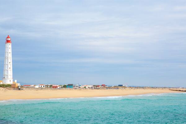 A coastal scene with a white lighthouse, sandy beach, and turquoise waters.