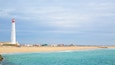 A coastal scene with a white lighthouse, sandy beach, and turquoise waters.