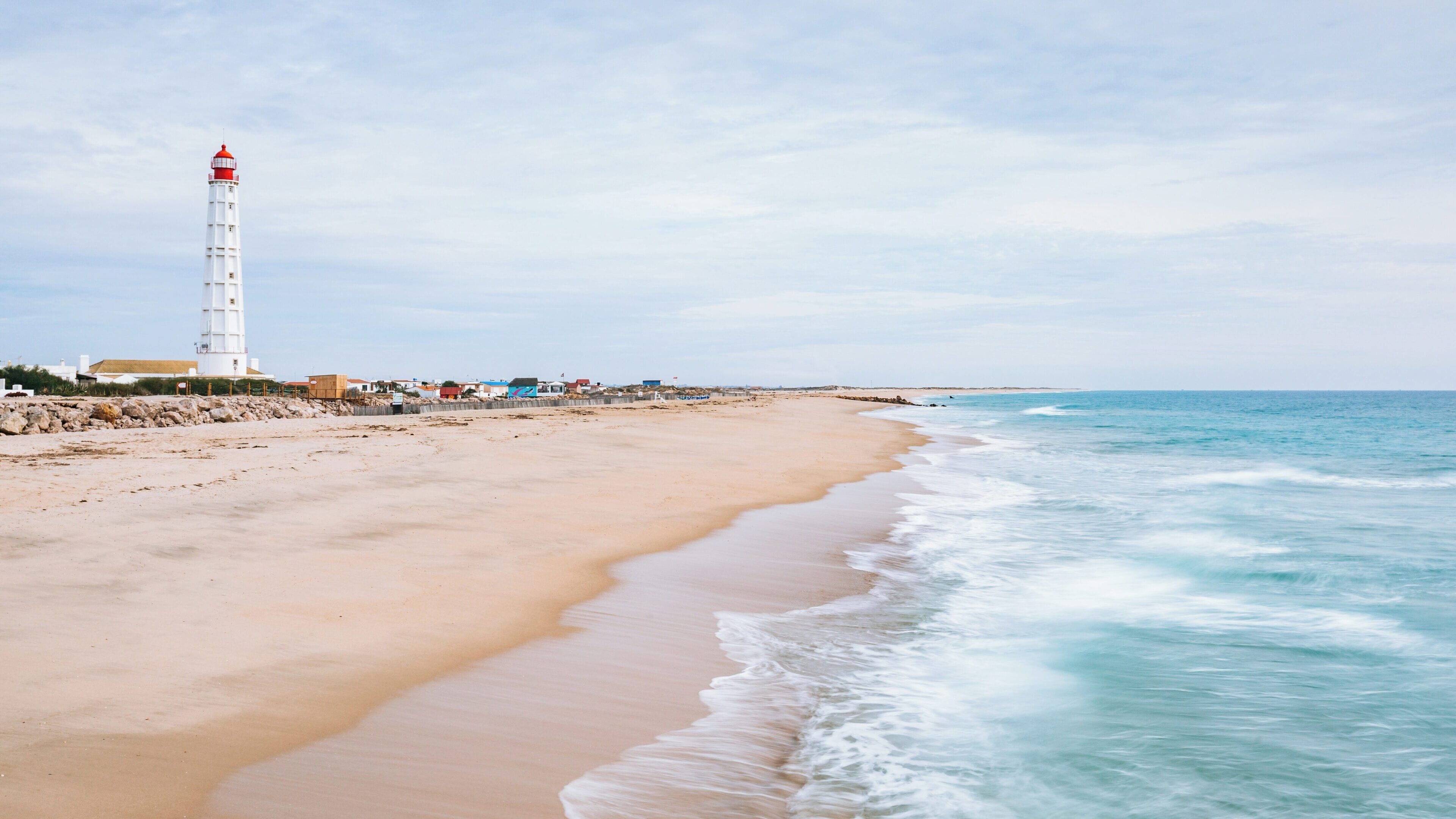 Faro Island Beach in Montenegro offers serene views of the shoreline and a striking lighthouse under cloudy skies