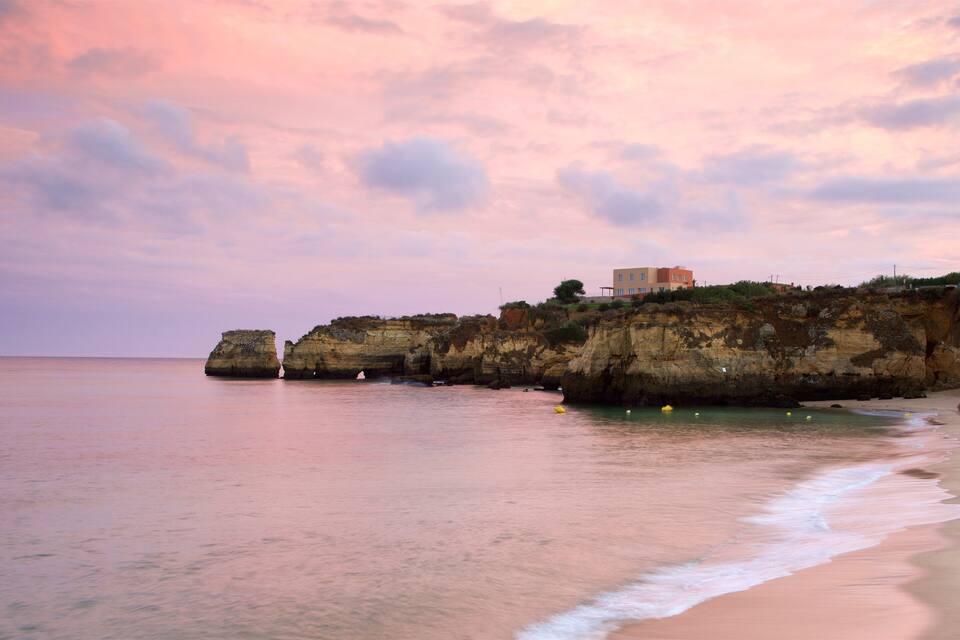 Paisagem costeira com falésias, uma praia e um edifício no topo das falésias.