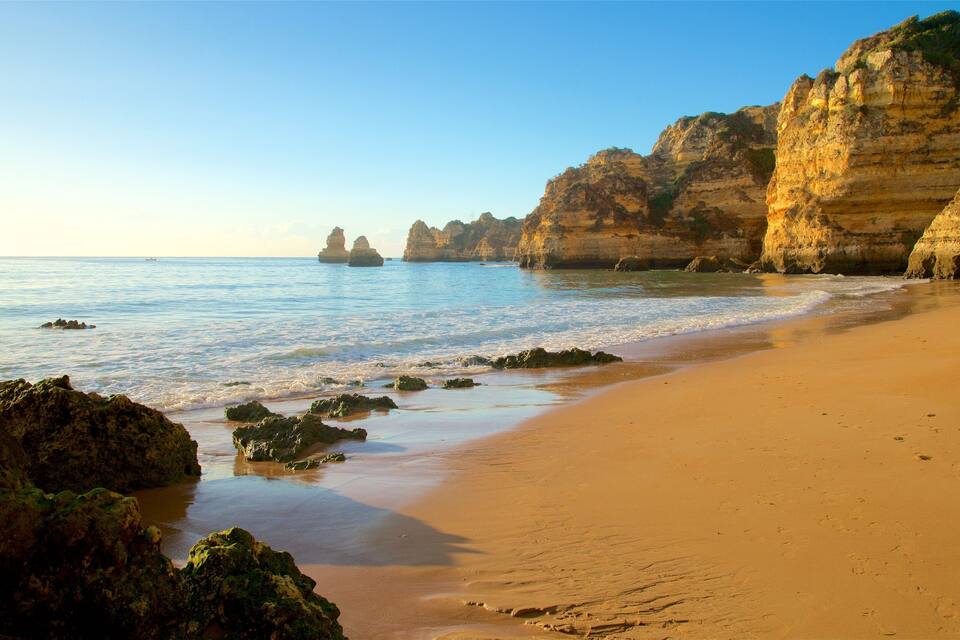 A sandy beach with rocky outcrops and cliffs in the background.