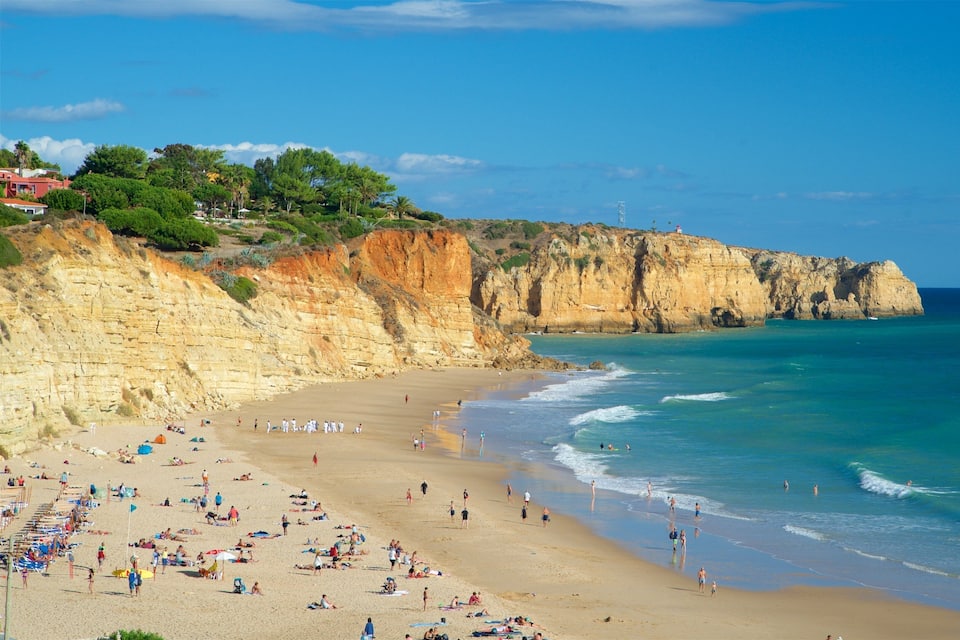 Una playa con gente tomando el sol y nadando, acantilados al fondo y un cielo azul despejado.