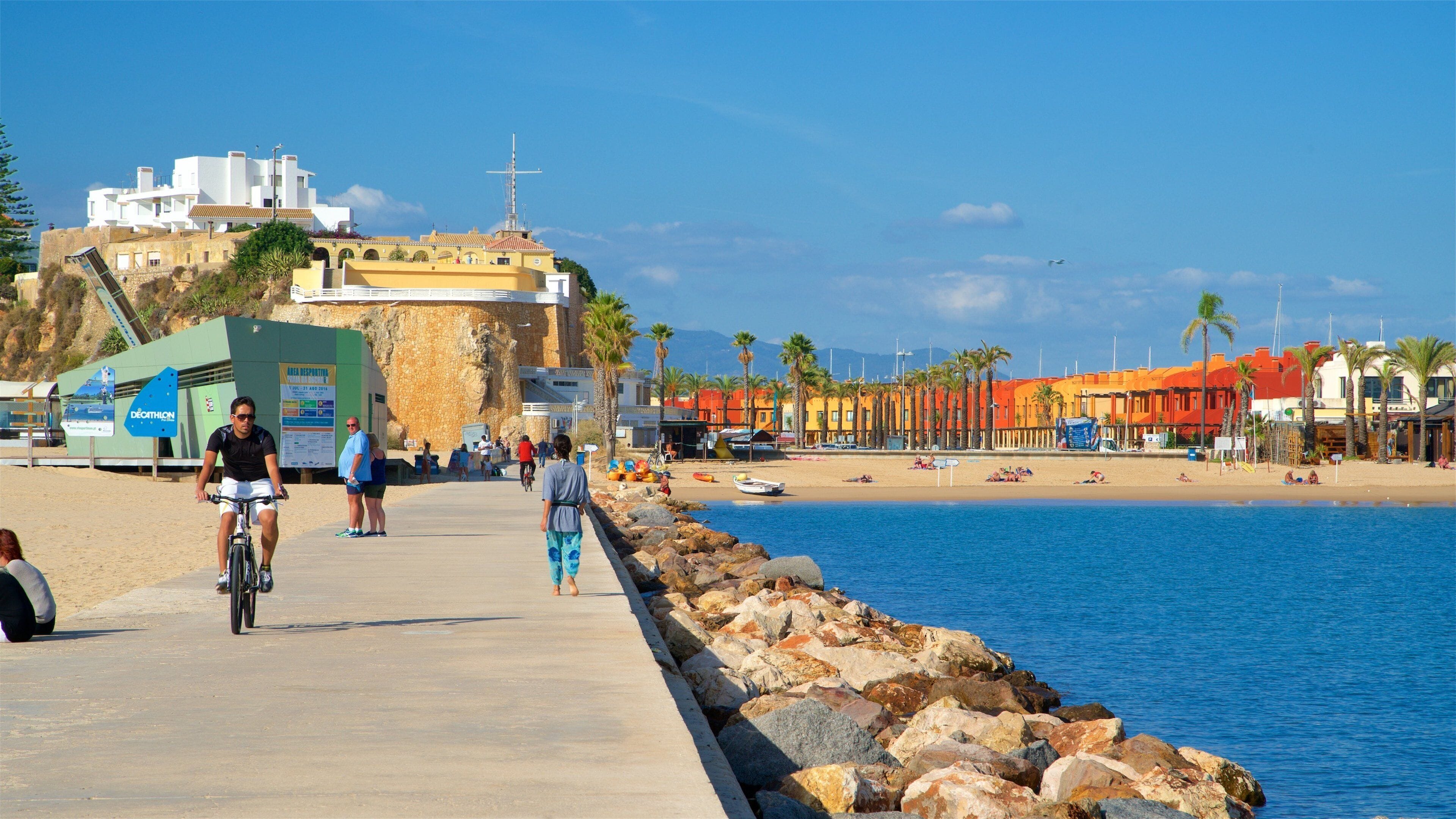 Una passejada marítima amb un tramuntanya rocosa, una platja i edificis de colors.
