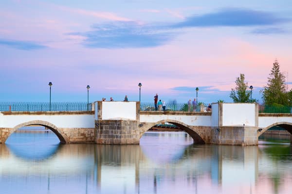 Eine Steinbrücke über einem ruhigen Fluss, auf der Menschen entlanggehen.