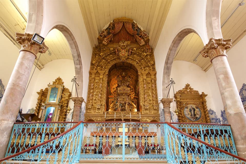 Een versierd religieus interieur met gouden altaars, een centraal beeld en blauwe balustrades.