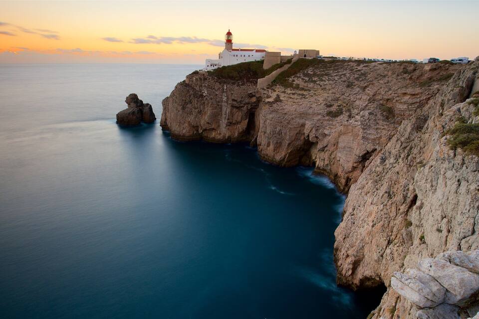 A coastal landscape with a lighthouse, rocky cliffs, and calm sea.
