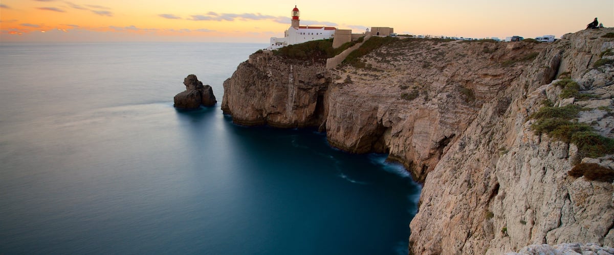 A coastal landscape with a lighthouse, rocky cliffs, and calm sea.