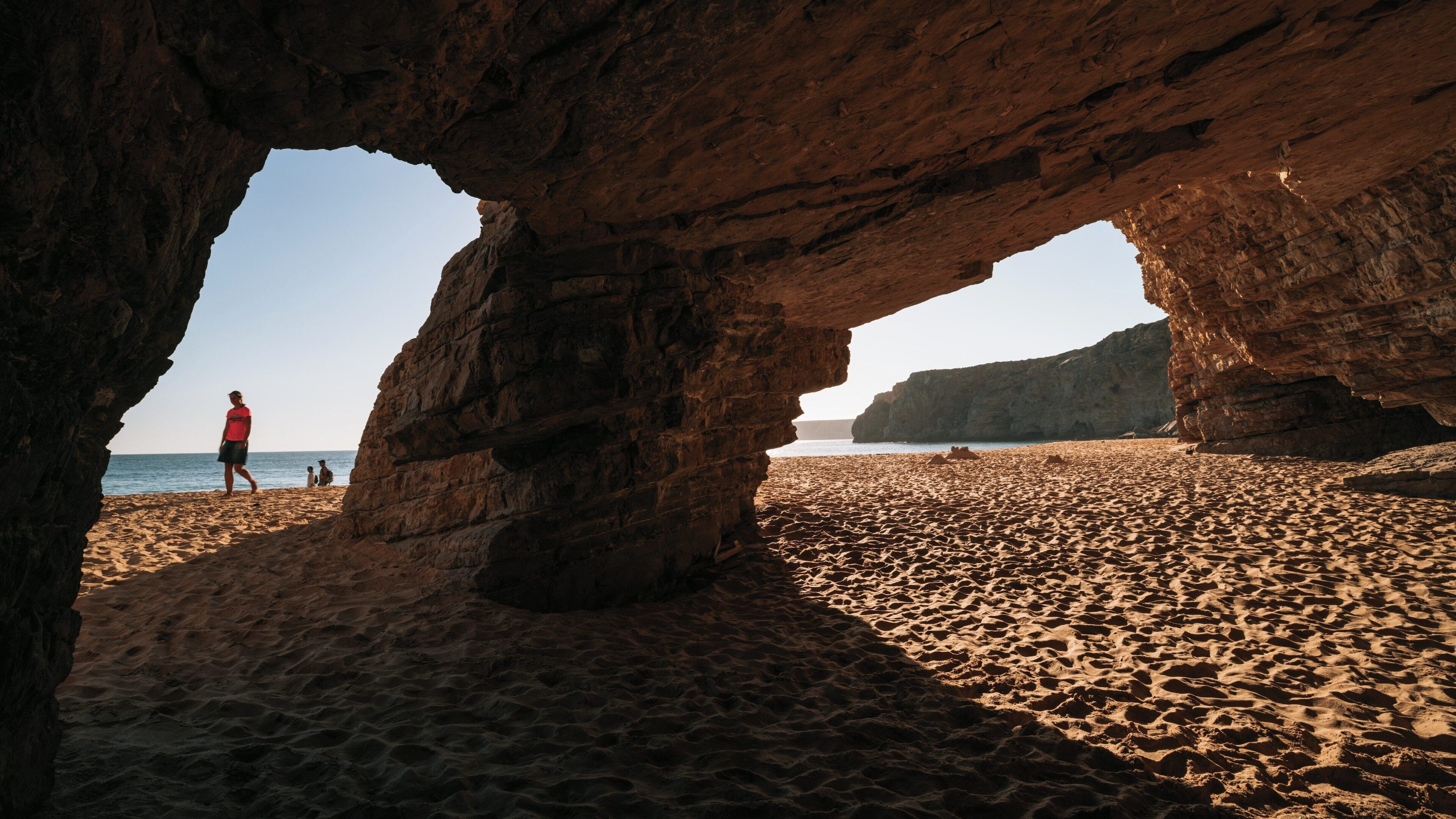 Stunning view from rock arch overlooking Beliche Beach in Sagres, Portugal revealing golden sands and calm waters in the background