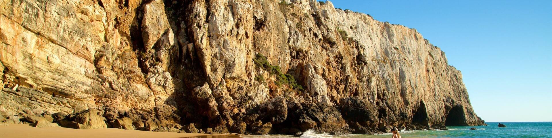 A rocky cliff by a beach with waves crashing against the shore.
