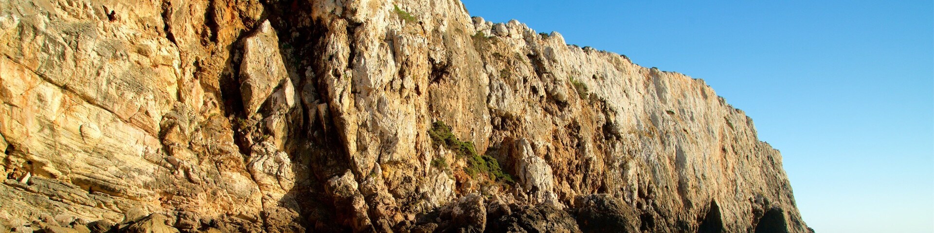 Un acantilado rocoso al borde de una playa, con olas rompiendo contra la orilla.