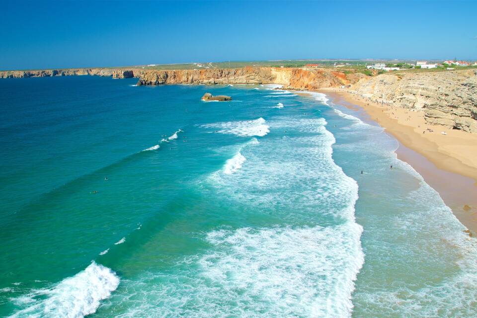 A coastal landscape with a sandy beach, clear turquoise waters, and rocky cliffs.