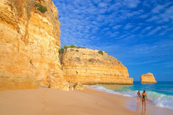 A sandy beach with a large cliff and a smaller rock formation in the water.