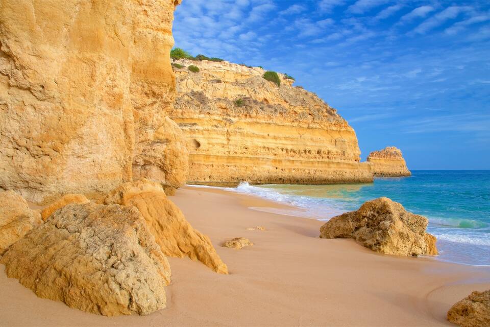 Una playa arenosa con grandes formaciones rocosas y acantilados al fondo.